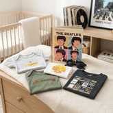Collection of Beatles-themed clothing and memorabilia on a crib in a nursery.
