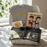Collection of Beatles-themed merchandise including t-shirts, a book, and sunglasses on a wooden surface.