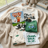 Collection of baby clothing and items with golf-themed designs on a textured surface.