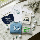 Children's clothing and accessories with golf-themed designs on a wooden surface.