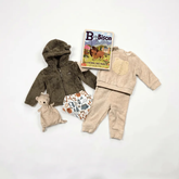 Children's clothing set with jacket, pants, teddy bear, and book on a white background
