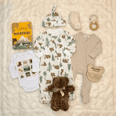 Collection of baby clothing and items on a textured surface with a 'Welcome Little One' sign.