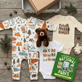 Baby clothing set with national park-themed designs on a wooden surface.