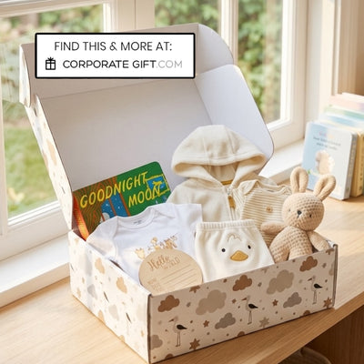 A baby gift box set on a wooden windowsill, containing a cream zip hoodie, a white t-shirt, a duck-themed diaper cover, a knitted bunny plush, and a 'Goodnight Moon' book. A white banner at the top reads 'FIND THIS & MORE AT: CORPORATE GIFT.