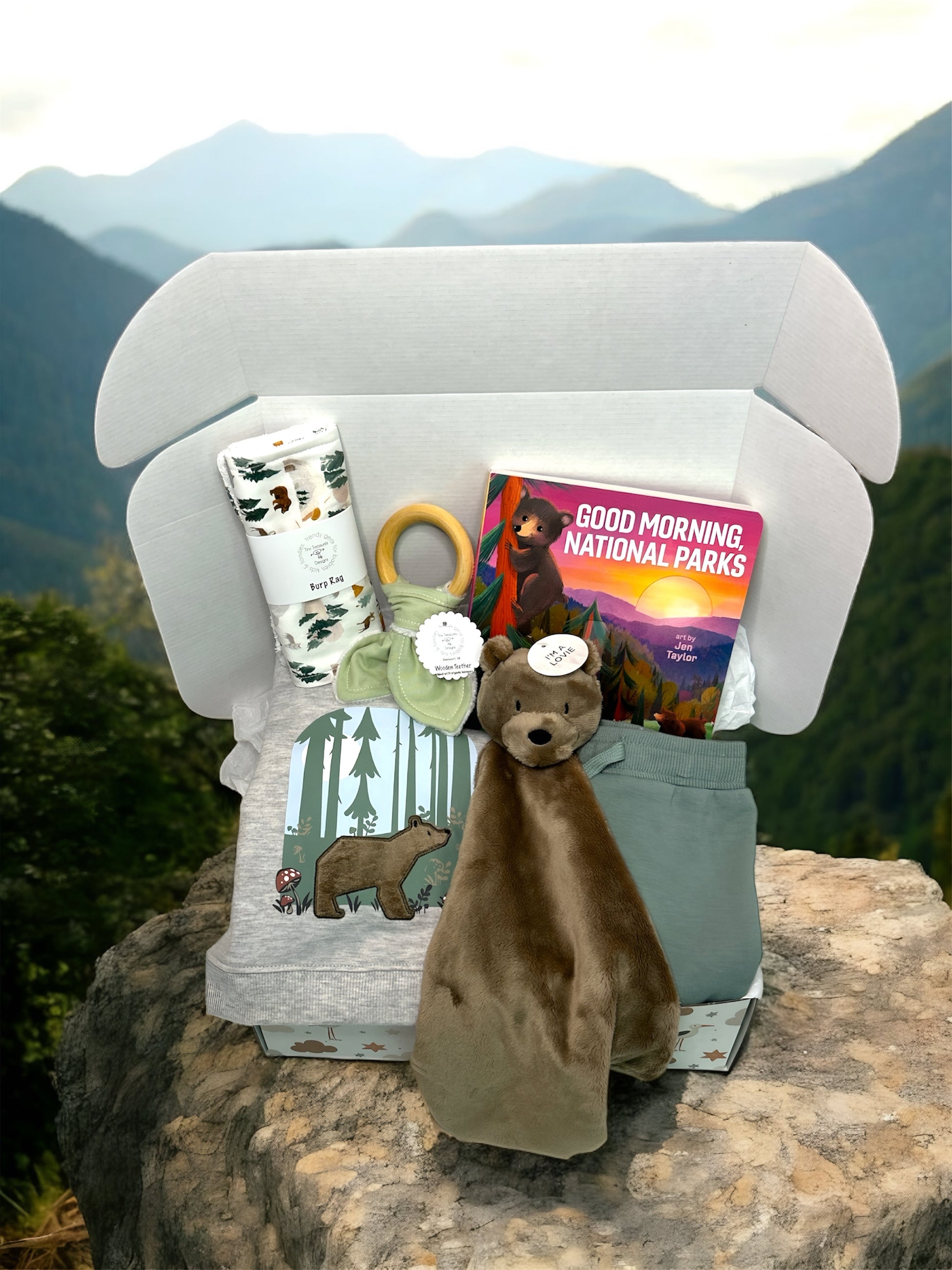 Children's gift set with books, a plush bear, and a mug on a rock with a mountain background