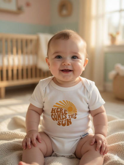 Baby sitting on a blanket wearing a onesie with 'Here Comes the Sun' text in a softly lit room.