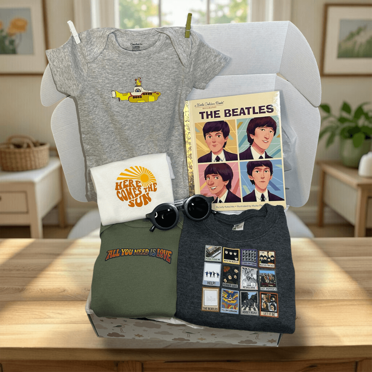 Collection of Beatles-themed merchandise including t-shirts, a baby onesie, and a notebook on a table.