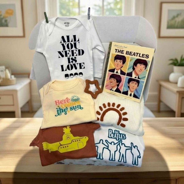 Collection of baby clothing and items with 'The Beatles' design on a table.