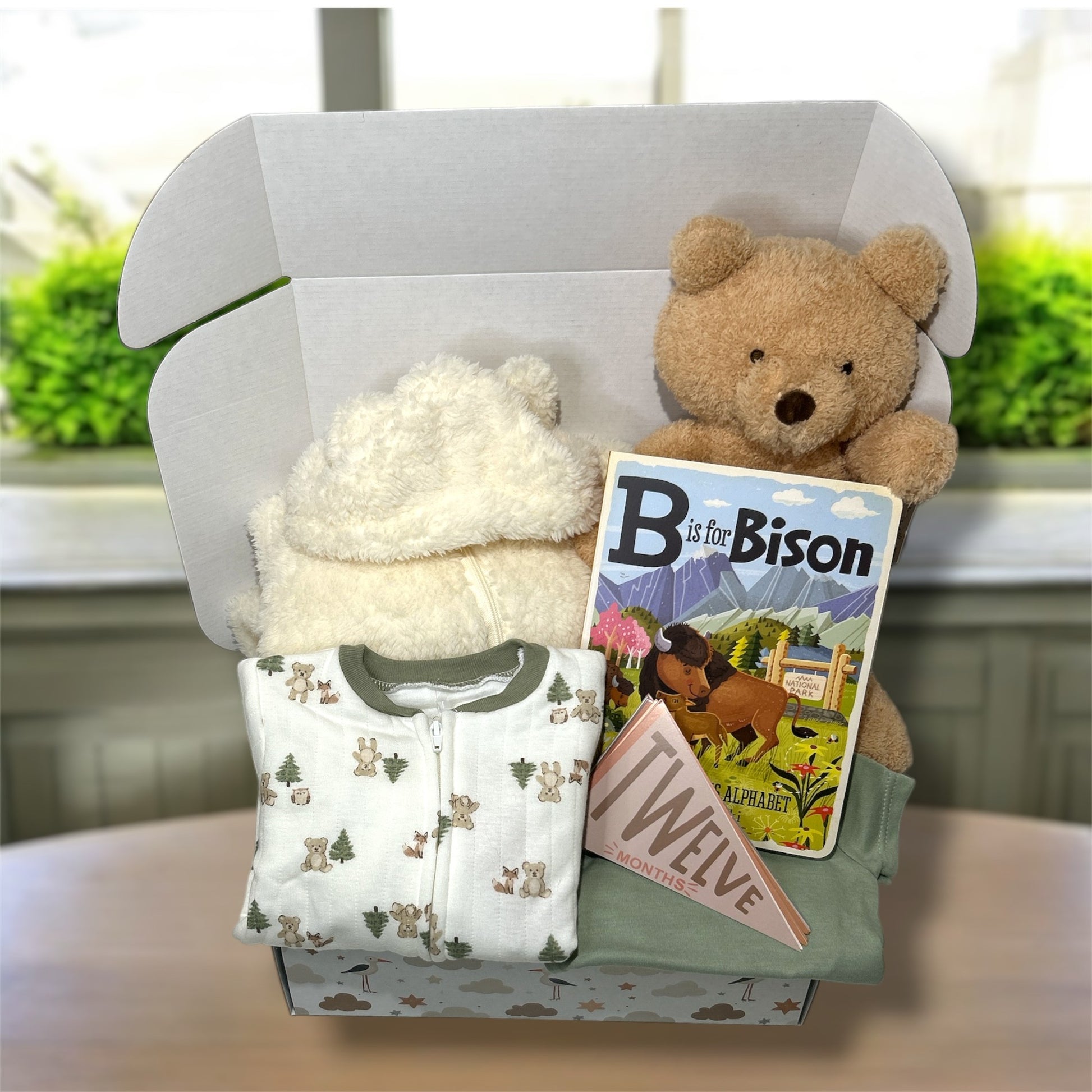 Gift box with teddy bear, children's book, and baby outfit on a neutral background