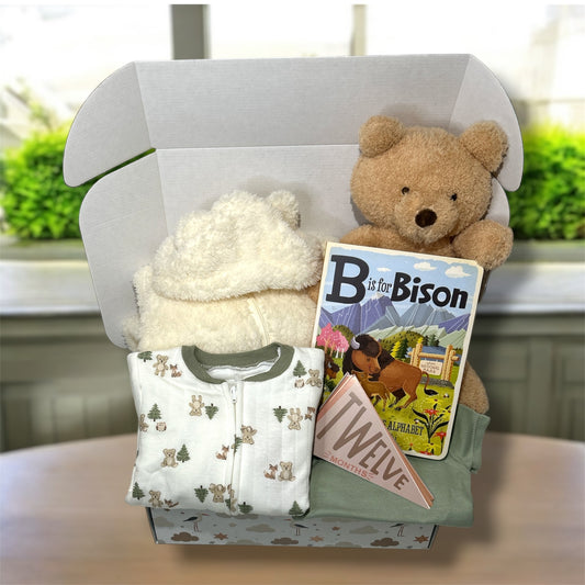 Gift box with teddy bear, children's book, and baby outfit on a neutral background