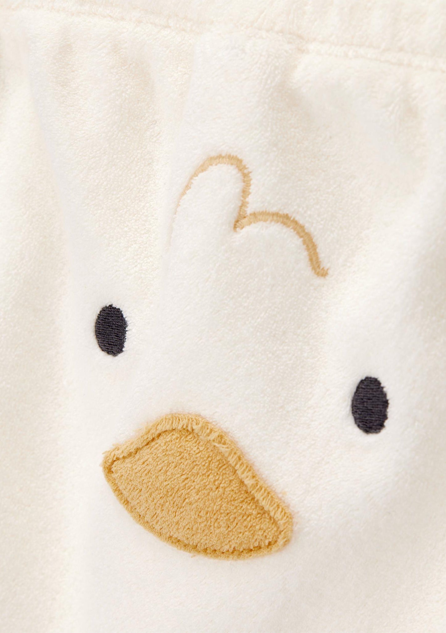 Close-up of a plush white fabric with a simple embroidered duck face, featuring a tan beak, black eyes, and a curved tan line above.