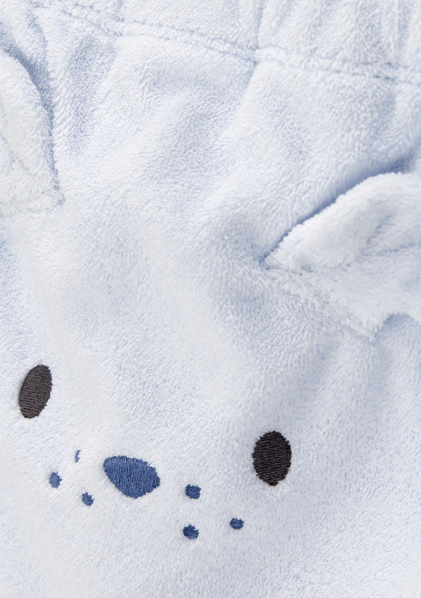 Close-up of a plush hooded garment in very light icy blue fabric, showing embroidered animal face details including black oval eyes, a blue nose, and small blue dots.