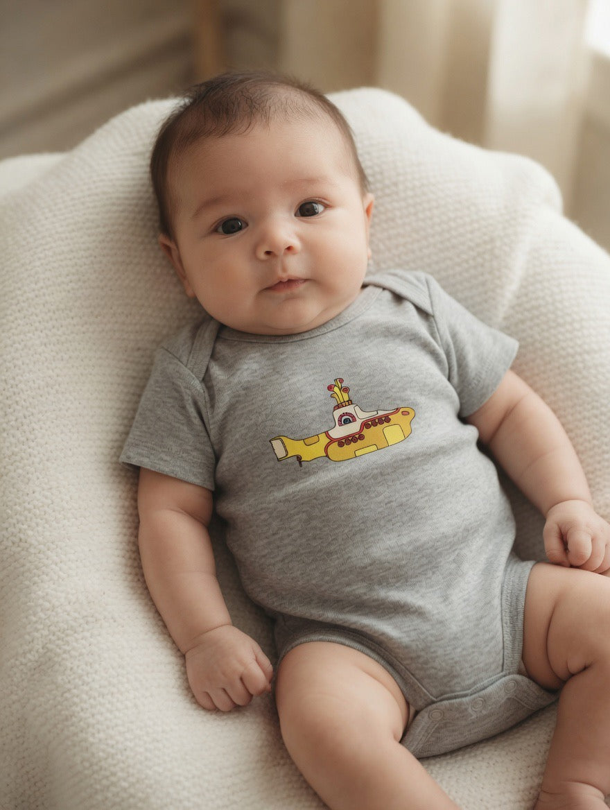 Baby wearing a gray onesie with a yellow submarine design on a soft surface.