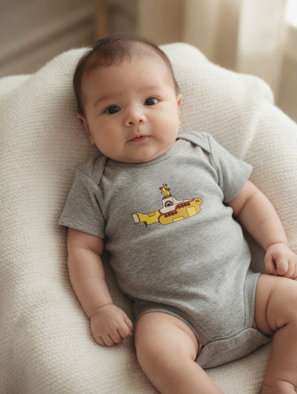 Baby wearing a gray onesie with a yellow submarine design on a soft surface.