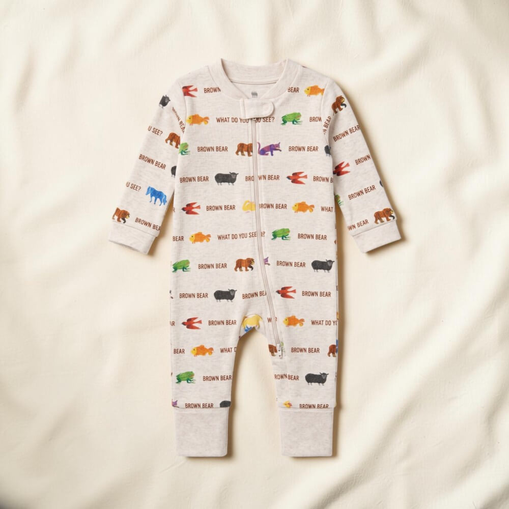 A baby long-sleeve footless one-piece romper in a light cream color, featuring an all-over print of colorful cartoon bears and the text 'BROWN BEAR' and 'WHAT DO YOU SEE?'. The romper is laid flat on a soft, textured off-white fabric background.