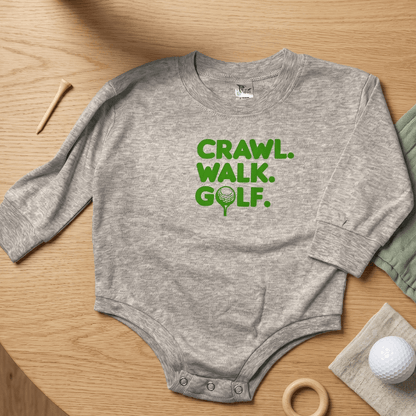 Gray baby onesie with 'CRAWL. WALK. GOLF.' text on a wooden surface with golf-themed items.