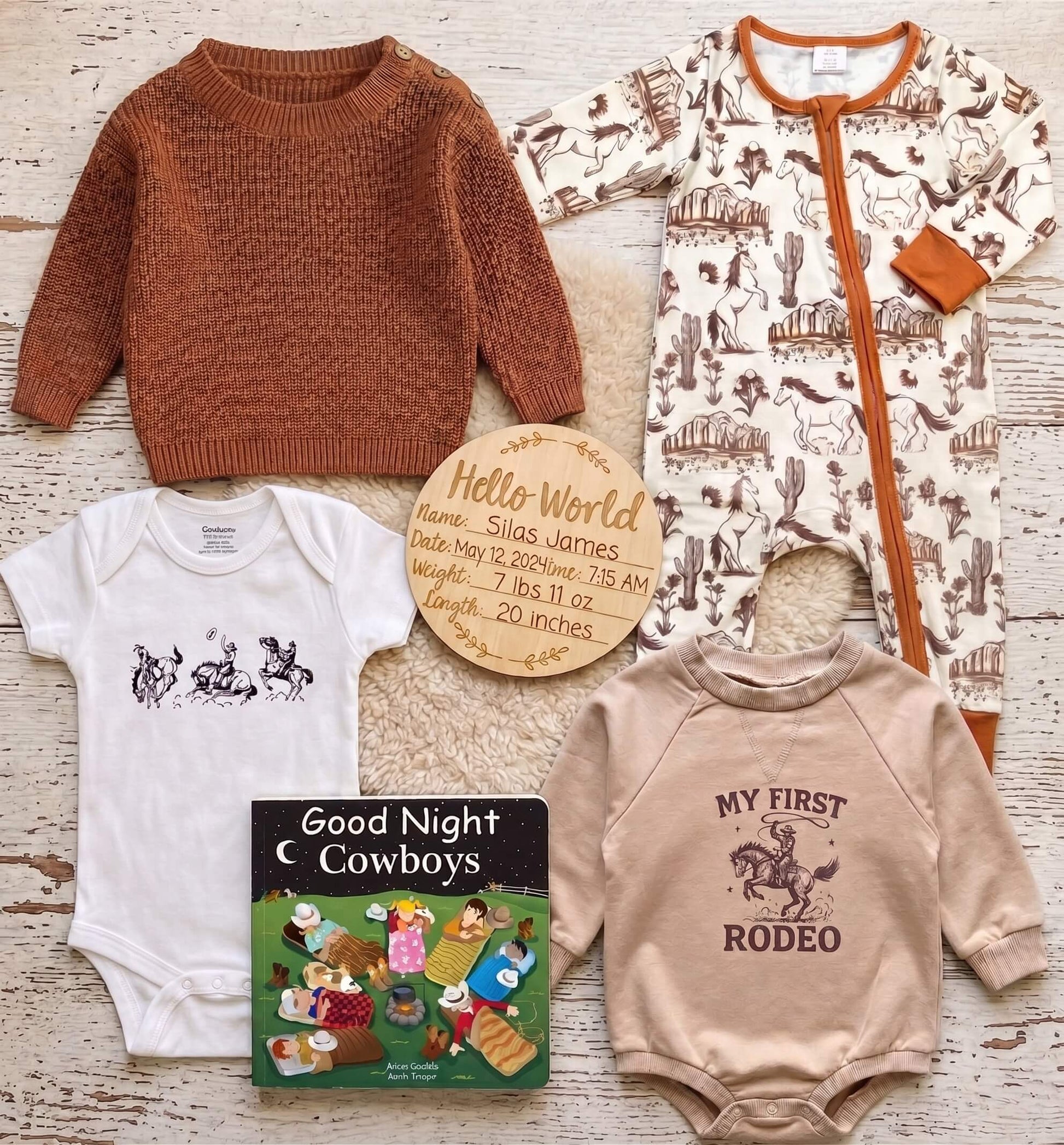 A baby gift set arranged on a whitewashed wood surface, including a rust-brown knit sweater, a cream one-piece with cowboy print, a white bodysuit with a horse-and-rider graphic, a beige long-sleeve shirt with a rodeo graphic, a personalized wooden name card, and a small 'Good Night Cowboys' book.