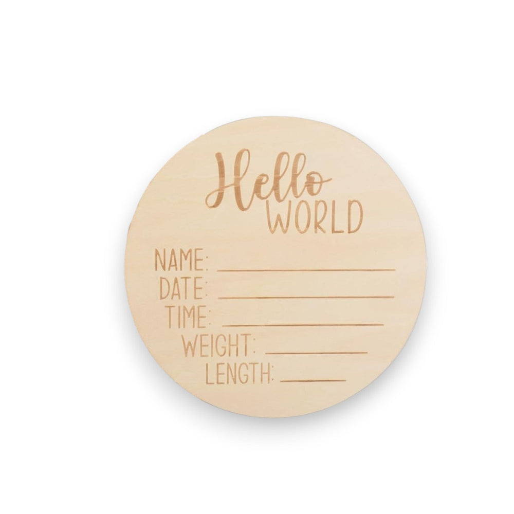 A round light wood baby milestone plaque engraved with 'Hello WORLD' and lines for writing name, date, time, weight, and length, shown on a clean white background.
