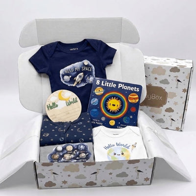 A baby gift box set containing a navy blue short-sleeve bodysuit with a space graphic, a book titled '8 Little Planets', a folded navy blue patterned blanket, a white 'Hello World' onesie, and a round wooden tag, all arranged inside an open patterned gift box.