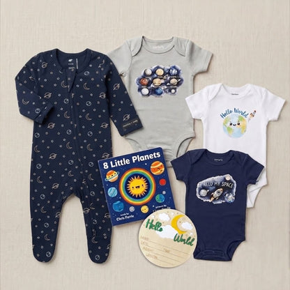 A baby gift set featuring four infant clothing pieces and two books on a light beige textured background: a navy footed sleeper with space motifs, a light gray bodysuit with a galaxy print, a white bodysuit with a cute Earth graphic and 'Hello World!' text, and a navy bodysuit with a space-themed graphic. A book titled '8 Little Planets' by Chris Facio and a round wooden name plaque are also included.