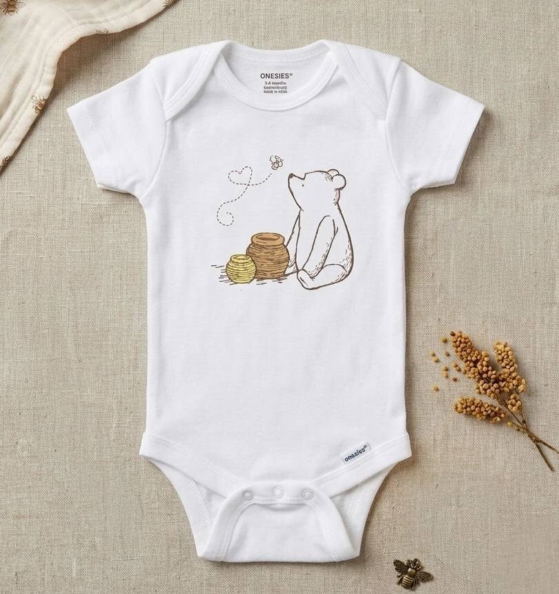 A white short-sleeve baby bodysuit laid flat on a beige linen background, featuring a printed illustration of a bear sitting beside a honey pot with a bee and heart detail. The brand name 'ONEEES' is visible inside the collar.
