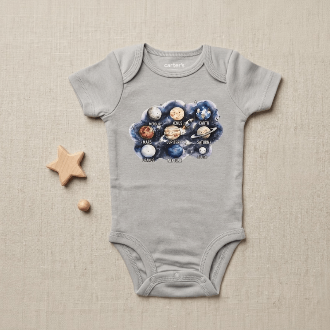 A light gray baby bodysuit with a colorful solar system graphic on the chest, displayed flat on a textured beige background with a wooden star and bead prop.
