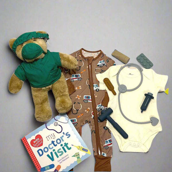 Teddy bear in doctor's outfit with baby onesie, stethoscope, toy book, and toy hammer on a gray background