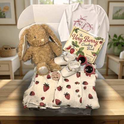 Baby gift set with plush toy, baby clothes, and book on a table.