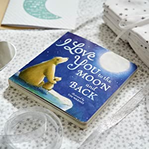 A children's book titled "I Love You to the Moon and Back" by Tim Warnies, featuring a blue night-sky cover with a polar bear and moon, styled on a star-patterned surface with ribbon and gift boxes nearby.