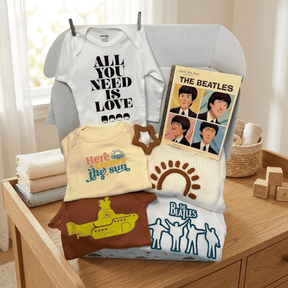 A coordinated baby clothing set displayed on a chair in a softly lit nursery-like setting. The set includes a white bodysuit with black text reading 'ALL YOU NEED IS LOVE,' a pale yellow top with 'Here is the sun,' a brown short-sleeve top with a yellow submarine graphic, a cream knit piece with a brown sun motif, and a white knit piece with blue figures, plus a Beatles album cover styled as part of the display.