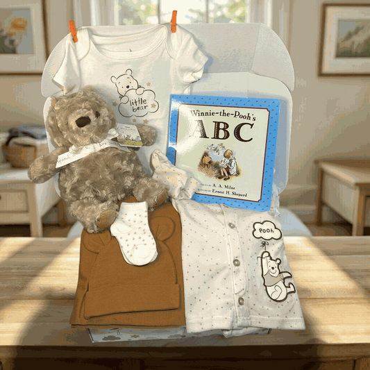 Baby gift set with teddy bear, clothes, and book on a table.