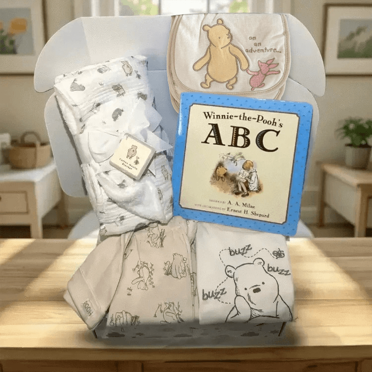 Baby gift set with blankets and a book titled 'Winnie-the-Pooh's ABC' on a wooden surface.
