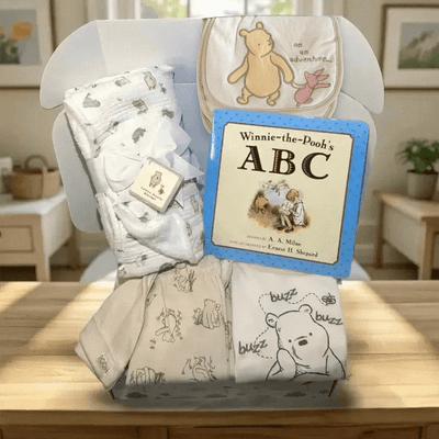 Baby gift set with blankets and a book titled 'Winnie-the-Pooh's ABC' on a wooden surface.