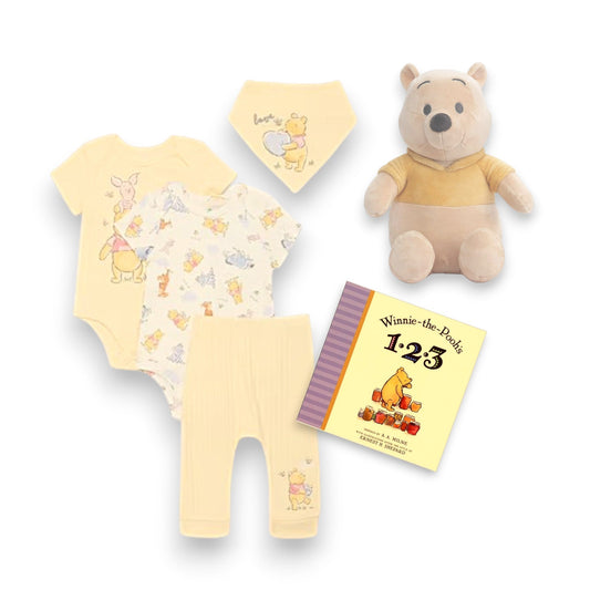 Winnie-the-Pooh baby clothing set with plush toy and book on a white background