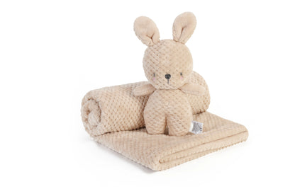 A beige textured plush bunny toy sitting on top of a matching rolled blanket and folded throw, photographed on a clean white background.