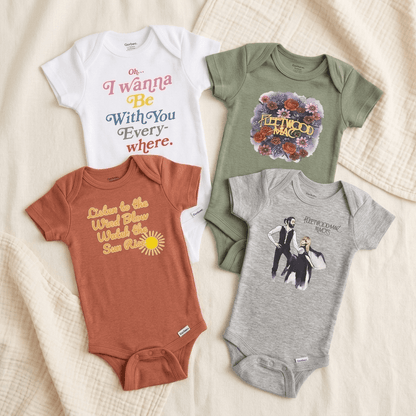 Four baby short-sleeve bodysuits arranged on a cream textured fabric background. The set includes a white bodysuit with multicolor text reading 'Oh I wanna Be With You Every where.