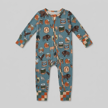 A baby long-sleeve footless one-piece jumpsuit in a dusty blue color, featuring an all-over print of bison, deer, mountains, and campfire scenes, finished with a front zipper and a checkered pattern on the cuffs and hem.