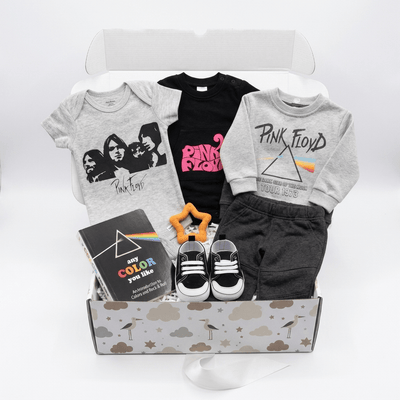A curated gift box set for kids featuring a gray band t-shirt, a black Pink Floyd t-shirt, a gray sweatshirt with a Pink Floyd prism graphic, black shorts, black and white sneakers, a book, and a star-shaped rattle inside a cloud-patterned box.