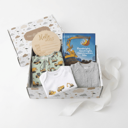 A baby gift box set on a white background, containing a white and gray baby clothing set, a construction-themed book, a wooden name card, and a patterned box with a cloud and star design.