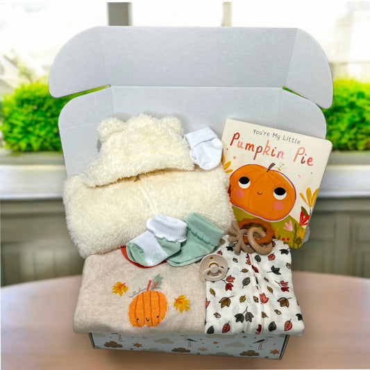 Baby gift set with plush toy, book, and clothes in a box on a table.
