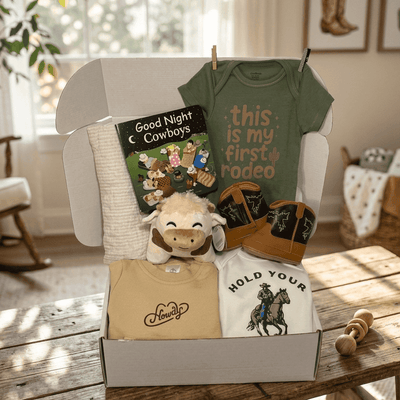 Baby gift set with t-shirts, a book, and plush toys on a wooden table.