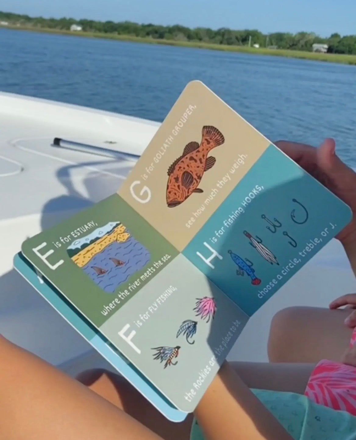 Person holding a colorful book with educational content by a body of water.