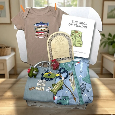 Collection of baby items including a onesie, bib, and bag with fishing-themed designs on a wooden surface.