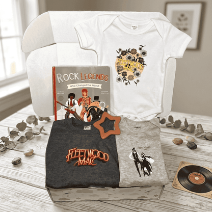 Fleetwood Mac-themed merchandise including t-shirts, a baby onesie, and a book on a wooden surface.