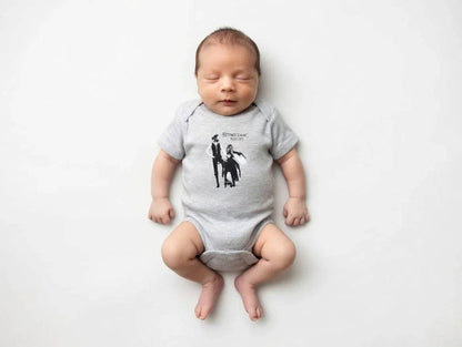 Newborn baby wearing a gray onesie with a graphic design on a white background