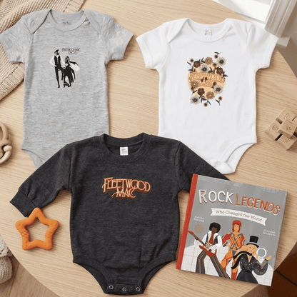 Three baby onesies with different designs on a wooden surface, accompanied by a book titled 'Rock Legends'.