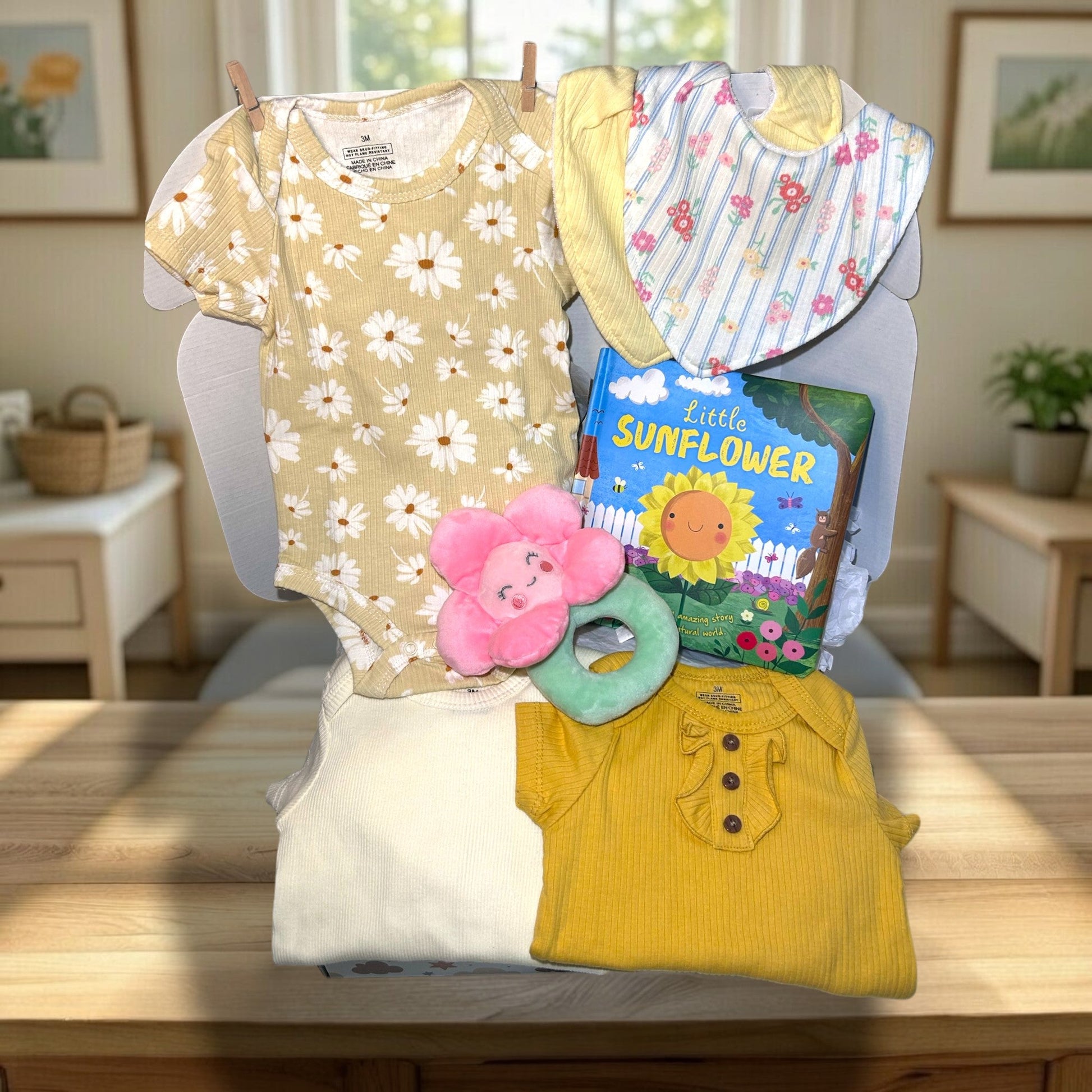 Baby clothing and toys on a table with a book titled 'Little Sunflower'.