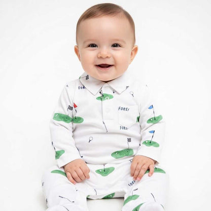 Baby wearing a white long-sleeved romper with a golf course print, featuring green fairways, flags, and "FORE!" text. Hey Baby Box.