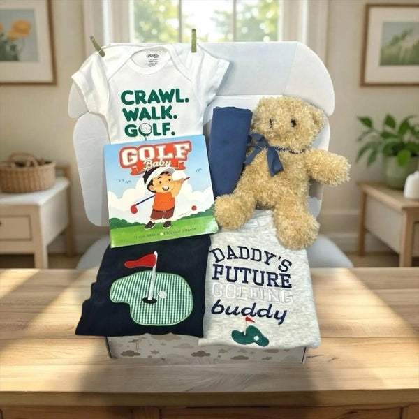 Baby gift set with t-shirt, onesie, book, and teddy bear on a chair.