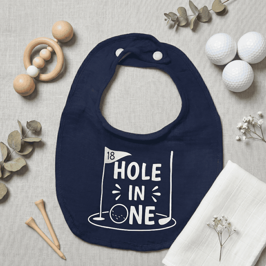 Navy blue bib with '18 Hole in One' print on a neutral background with golf-themed items.